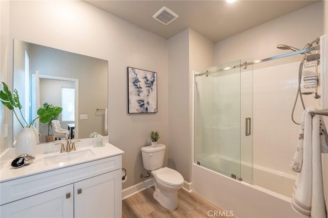 full bathroom with combined bath / shower with glass door, hardwood / wood-style floors, vanity, and toilet