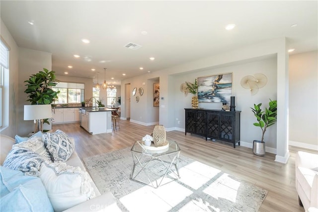 living room featuring a notable chandelier, light wood-type flooring, and sink