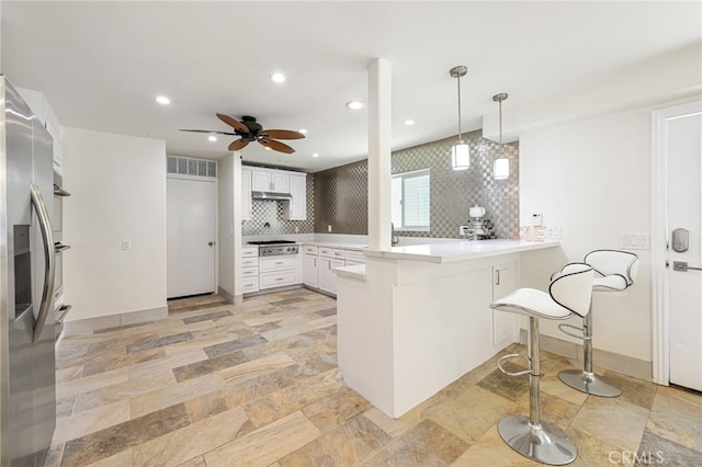 kitchen with kitchen peninsula, decorative backsplash, stainless steel appliances, decorative light fixtures, and white cabinets