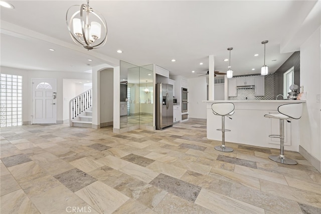 kitchen featuring gray cabinetry, tasteful backsplash, a kitchen breakfast bar, ceiling fan with notable chandelier, and appliances with stainless steel finishes