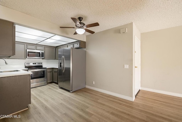 kitchen featuring appliances with stainless steel finishes, a textured ceiling, ceiling fan, sink, and light hardwood / wood-style floors