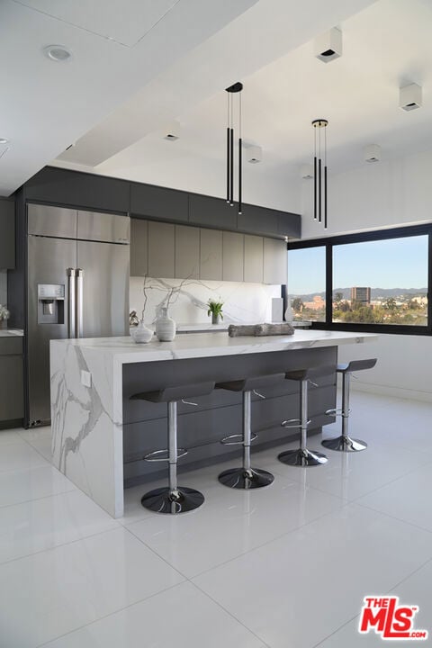 kitchen featuring stainless steel built in refrigerator, backsplash, pendant lighting, a breakfast bar area, and light tile patterned floors