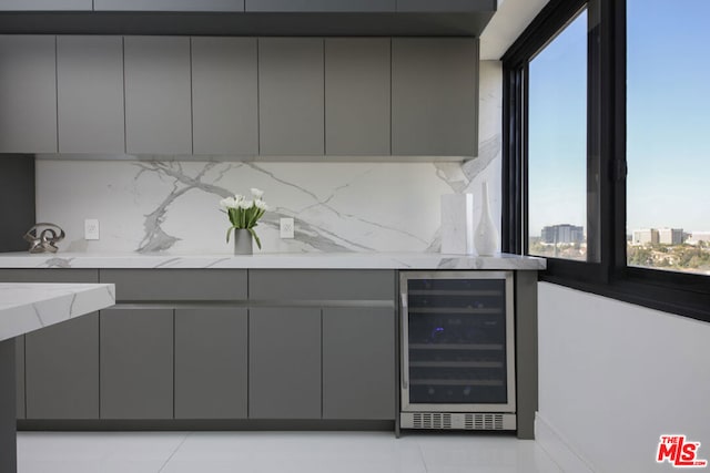 kitchen featuring backsplash, gray cabinets, light stone counters, and beverage cooler