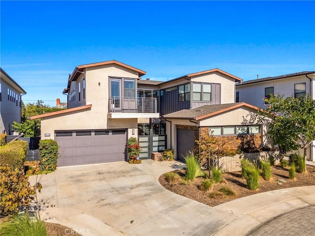 contemporary house featuring a garage, driveway, a balcony, and stucco siding