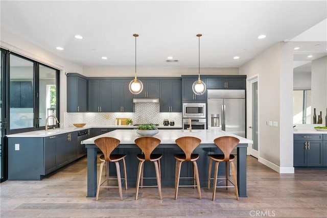 kitchen with built in appliances, hanging light fixtures, a kitchen island, and light hardwood / wood-style floors