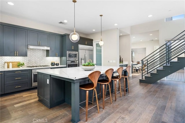 kitchen with light stone countertops, a kitchen island, decorative light fixtures, and built in appliances