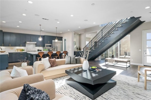 living area with recessed lighting, visible vents, baseboards, stairs, and light wood-type flooring