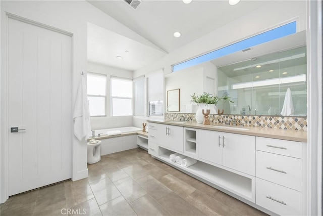 full bath featuring double vanity, visible vents, lofted ceiling, a garden tub, and a sink