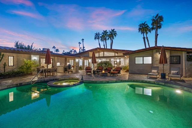 pool at dusk featuring an in ground hot tub and a patio