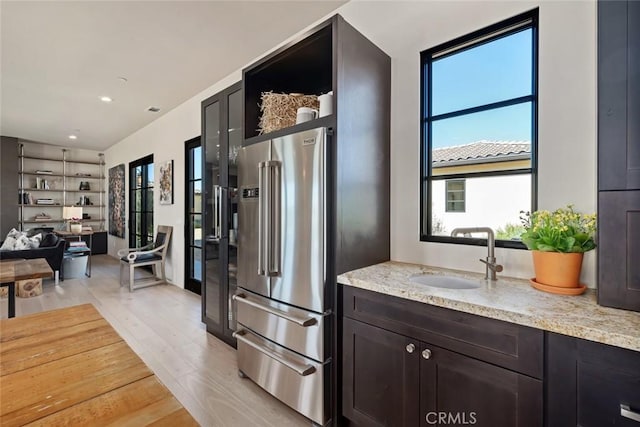 kitchen featuring sink, light hardwood / wood-style flooring, light stone countertops, high quality fridge, and dark brown cabinetry