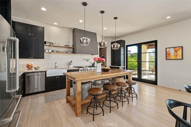 kitchen with pendant lighting, ventilation hood, sink, light hardwood / wood-style flooring, and stainless steel appliances