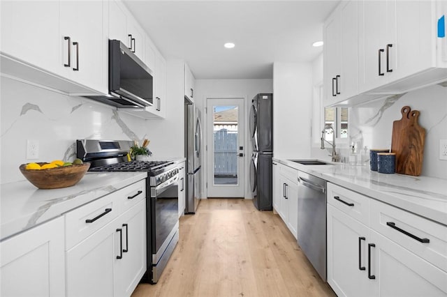 kitchen with sink, light wood-type flooring, light stone counters, white cabinetry, and stainless steel appliances