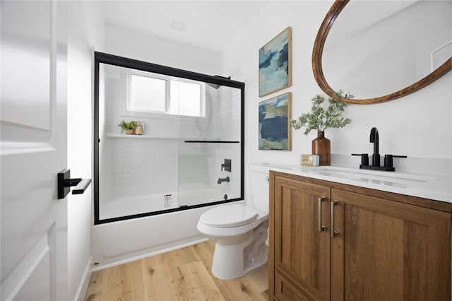 full bathroom with combined bath / shower with glass door, vanity, hardwood / wood-style flooring, and toilet