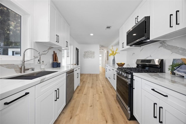 kitchen with white cabinets, sink, light stone countertops, light wood-type flooring, and appliances with stainless steel finishes