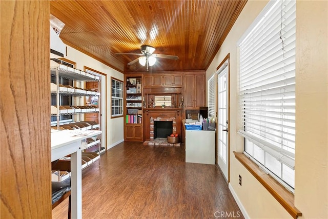 office space featuring ceiling fan, dark wood-type flooring, wooden ceiling, a brick fireplace, and crown molding