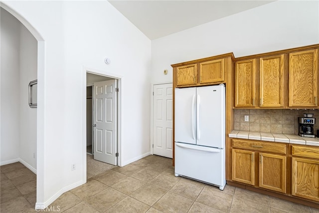 kitchen with a high ceiling, tasteful backsplash, tile countertops, white fridge, and light tile patterned flooring