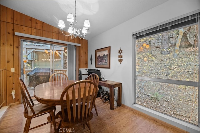 dining room featuring an inviting chandelier, light hardwood / wood-style floors, vaulted ceiling, and wooden walls