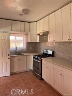 kitchen with sink, stainless steel stove, decorative backsplash, light tile patterned flooring, and white cabinetry