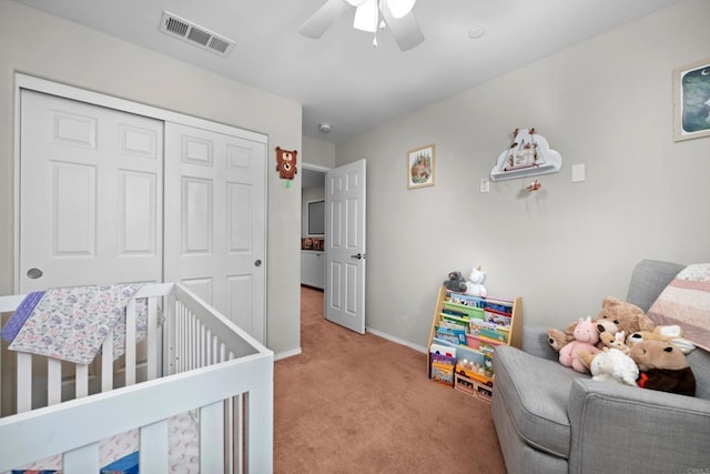 carpeted bedroom with ceiling fan, a crib, and a closet