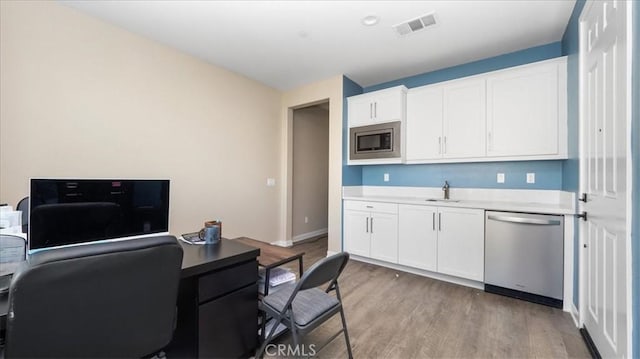 kitchen with sink, white cabinets, light wood-type flooring, and appliances with stainless steel finishes