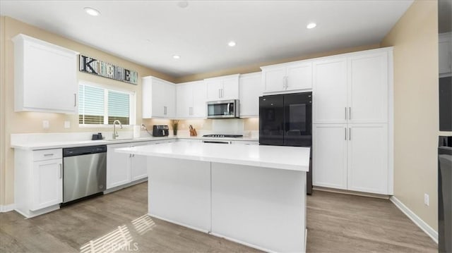 kitchen featuring stainless steel appliances, sink, light hardwood / wood-style flooring, white cabinets, and a kitchen island