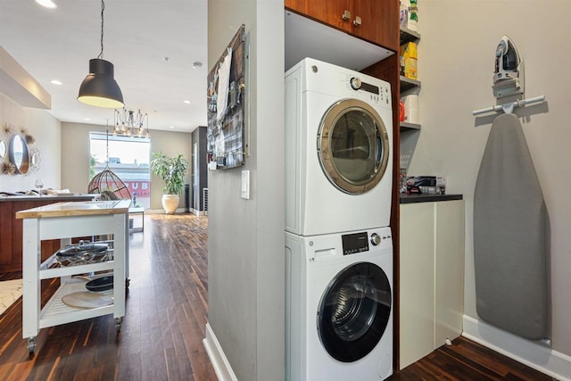 laundry area with an inviting chandelier, stacked washer / dryer, and dark wood-type flooring