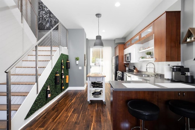 kitchen with sink, dark hardwood / wood-style floors, kitchen peninsula, a breakfast bar, and appliances with stainless steel finishes