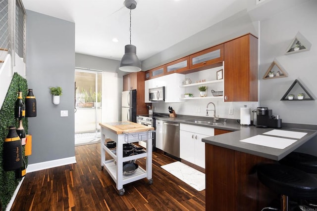 kitchen featuring kitchen peninsula, appliances with stainless steel finishes, dark wood-type flooring, sink, and pendant lighting