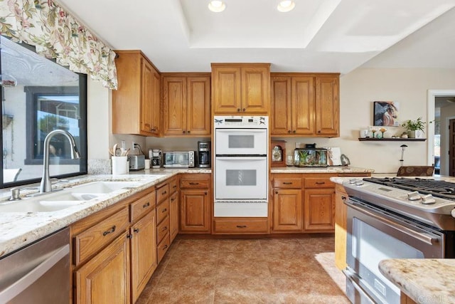 kitchen featuring light stone countertops, sink, a tray ceiling, light tile patterned flooring, and appliances with stainless steel finishes