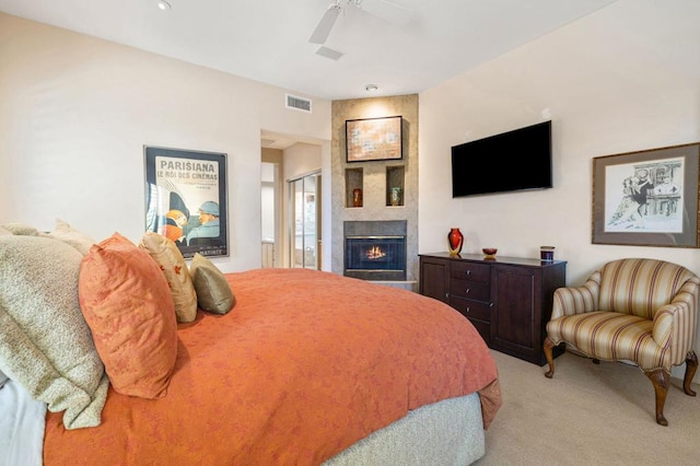 bedroom with ceiling fan, light colored carpet, and a tiled fireplace