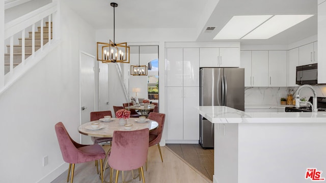 kitchen with backsplash, light wood-type flooring, white cabinetry, kitchen peninsula, and stainless steel refrigerator