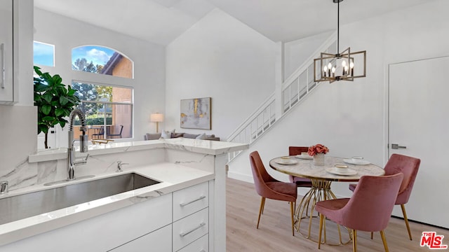 kitchen with white cabinets, sink, hanging light fixtures, light wood-type flooring, and a chandelier