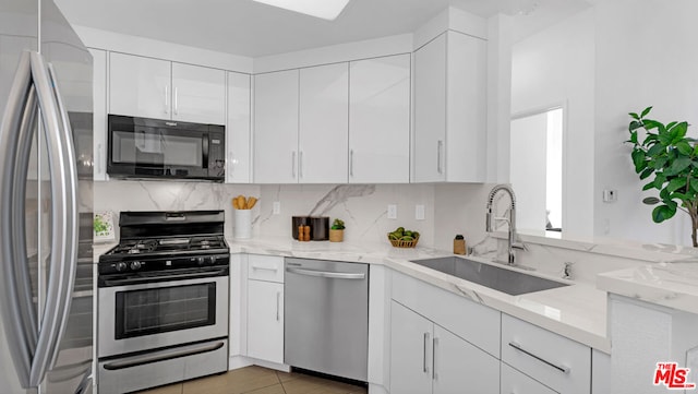 kitchen with light stone countertops, sink, decorative backsplash, white cabinets, and appliances with stainless steel finishes