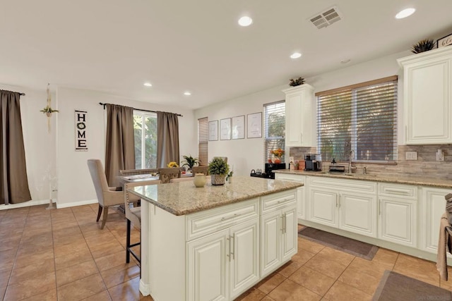 kitchen with decorative backsplash, a center island, light stone countertops, and sink