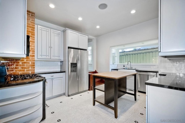 kitchen with appliances with stainless steel finishes, backsplash, sink, light tile patterned floors, and white cabinets