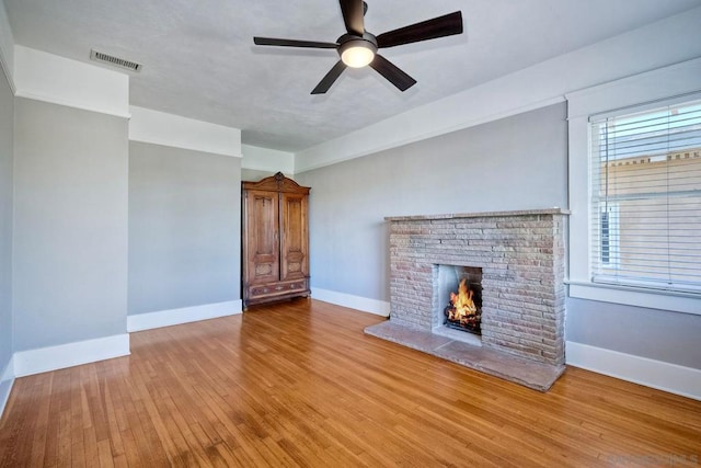 unfurnished living room with a brick fireplace, ceiling fan, and light wood-type flooring