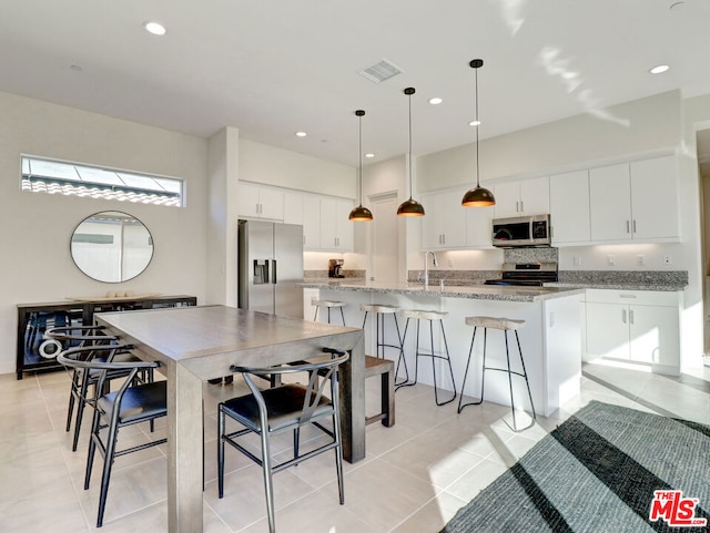 kitchen with appliances with stainless steel finishes, light stone counters, decorative light fixtures, a center island with sink, and white cabinets