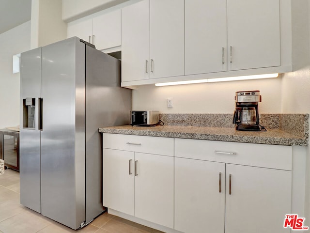 kitchen with beverage cooler, light tile patterned floors, light stone counters, stainless steel fridge, and white cabinets