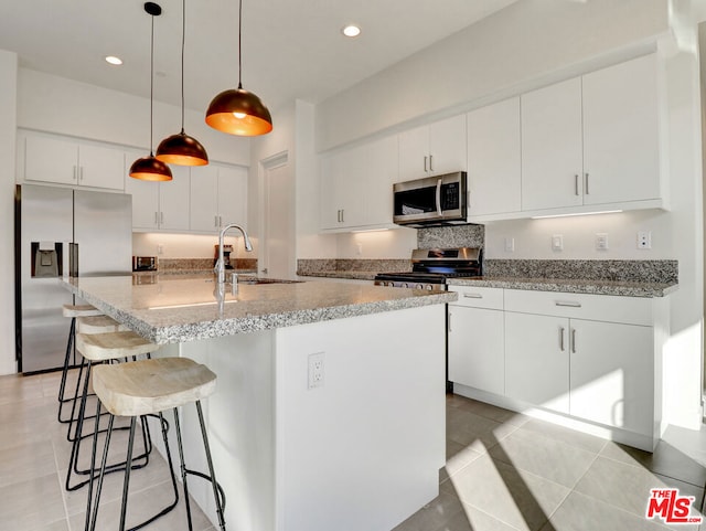 kitchen with white cabinets, decorative light fixtures, an island with sink, and appliances with stainless steel finishes