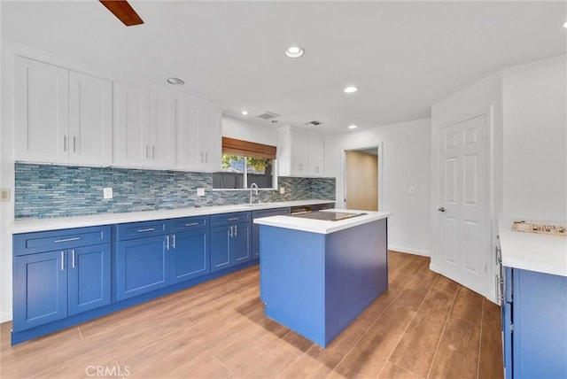 kitchen with blue cabinetry, white cabinetry, a center island, sink, and light hardwood / wood-style flooring