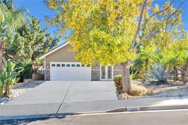 view of property hidden behind natural elements featuring driveway, stone siding, and a garage