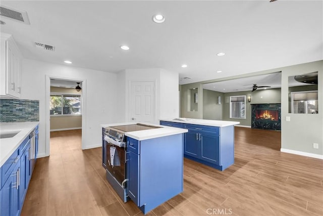 kitchen with blue cabinets, a kitchen island, open floor plan, light countertops, and stainless steel range with electric stovetop