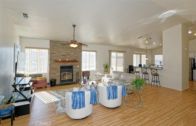 living room with vaulted ceiling, ceiling fan, a stone fireplace, and light hardwood / wood-style floors