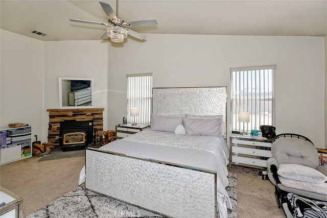 carpeted bedroom featuring ceiling fan, a stone fireplace, vaulted ceiling, and multiple windows