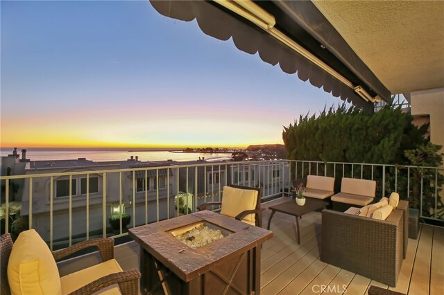 deck at dusk featuring a water view and an outdoor living space with a fire pit