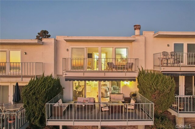 back house at dusk featuring outdoor lounge area and a balcony