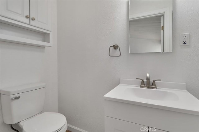 bathroom featuring toilet, a textured wall, baseboards, and vanity