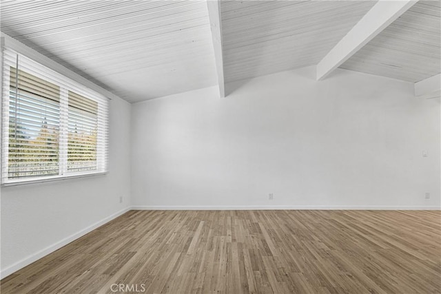 empty room featuring vaulted ceiling with beams, wood finished floors, and baseboards