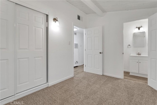 unfurnished bedroom featuring connected bathroom, light carpet, sink, and vaulted ceiling with beams