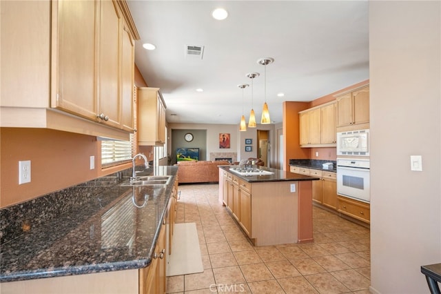 kitchen with a center island, white appliances, sink, hanging light fixtures, and light brown cabinetry